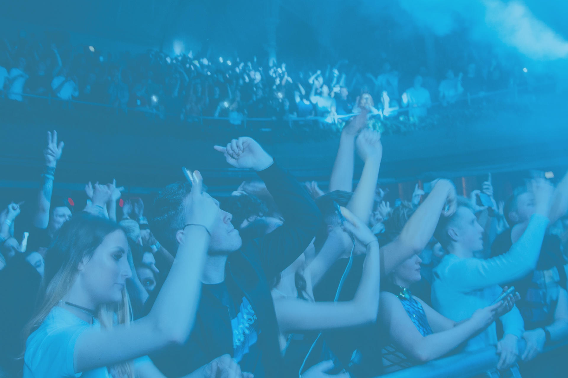 Público disfrutando de un concierto con los brazos en alto bajo luces azules en Gran Canaria